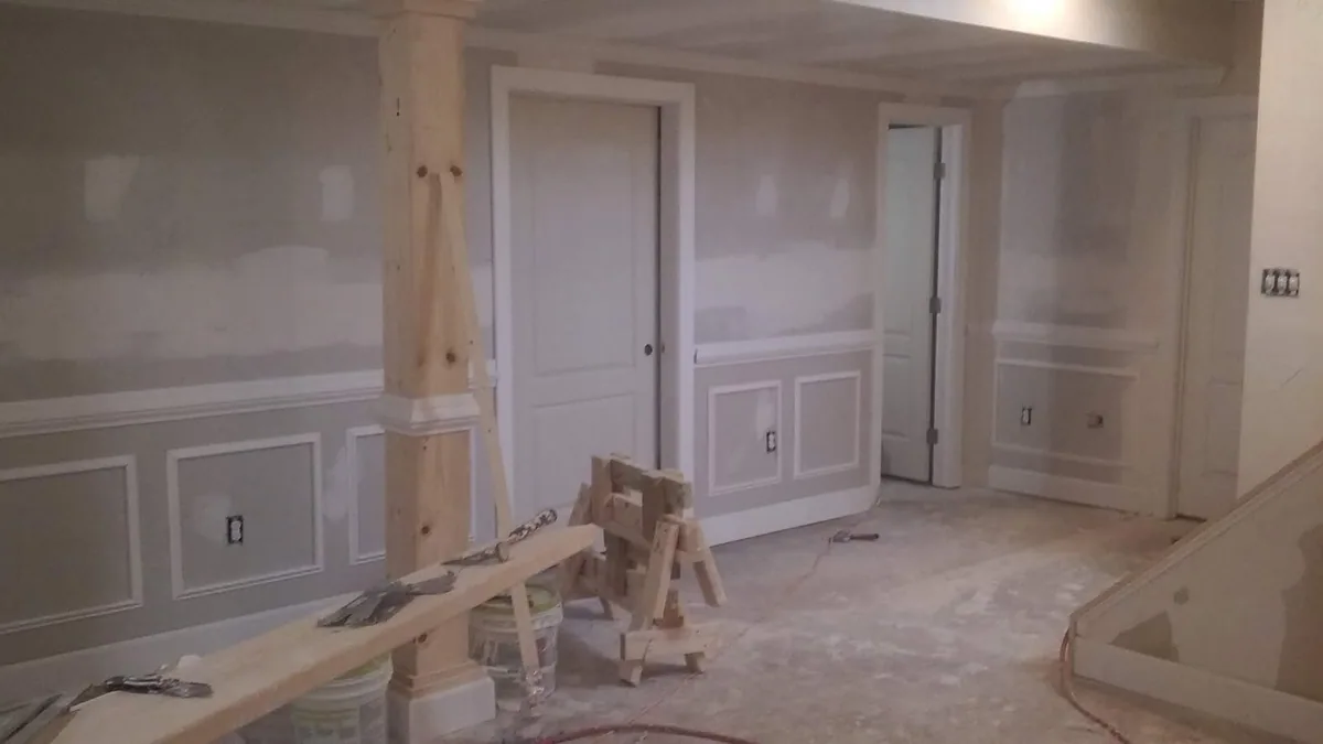 Basement remodel in progress with paneled wall trim and unfinished columns