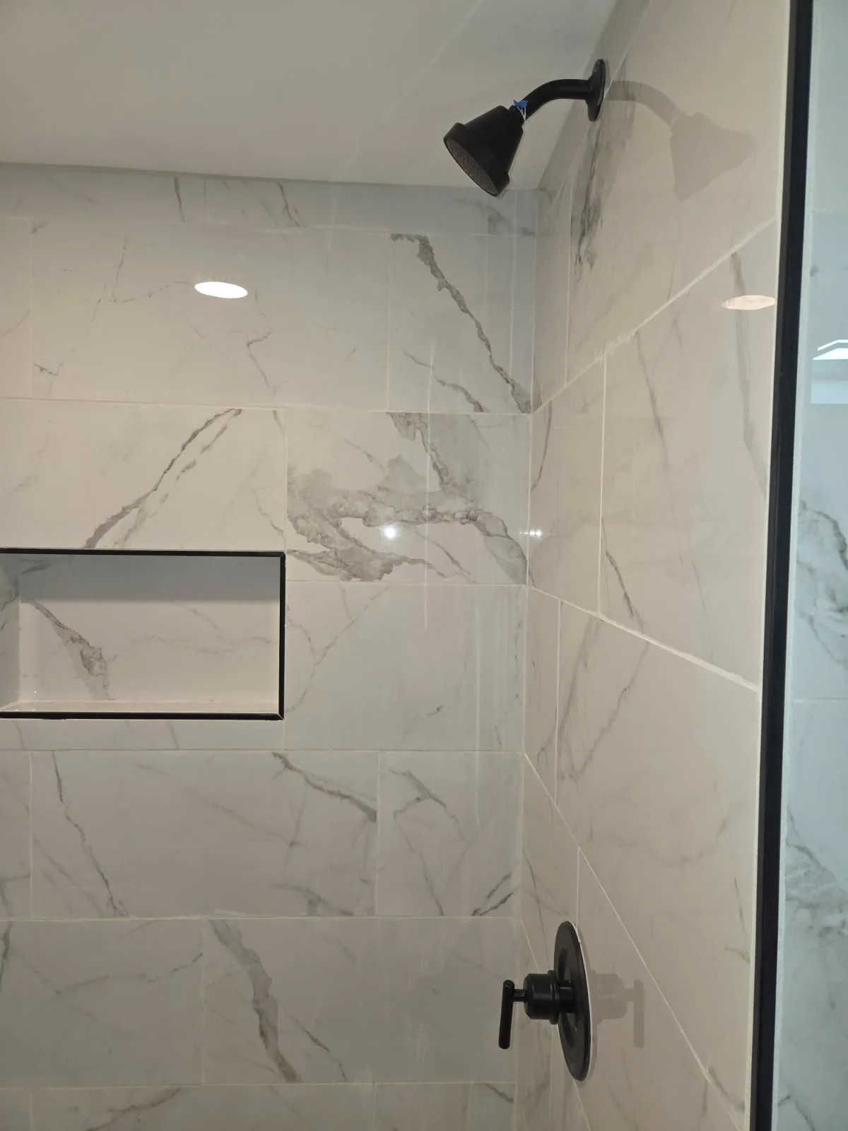 Tiled shower with black fixtures and a recessed wall niche