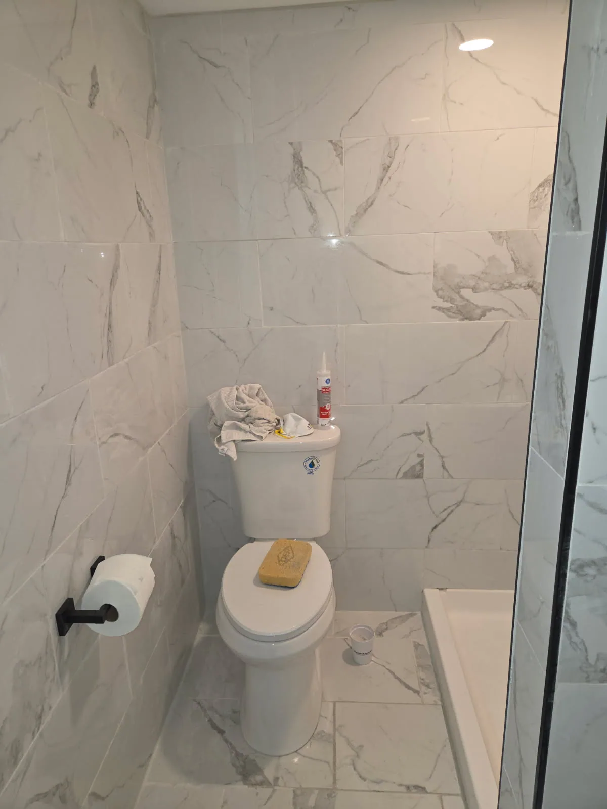 Bathroom with marble-look wall and floor tile beside a glass shower enclosure