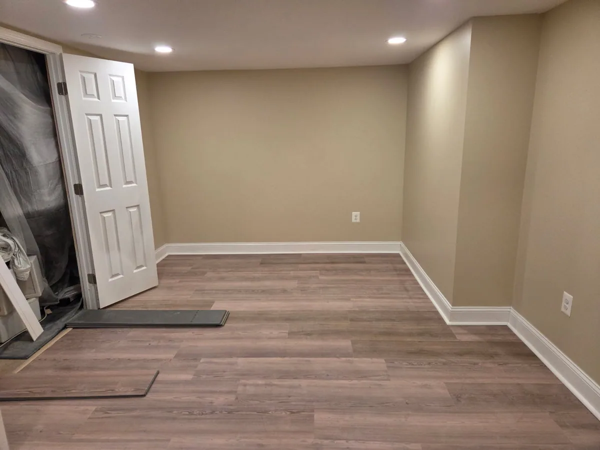 Finished basement room showing recessed lighting and newly installed plank flooring