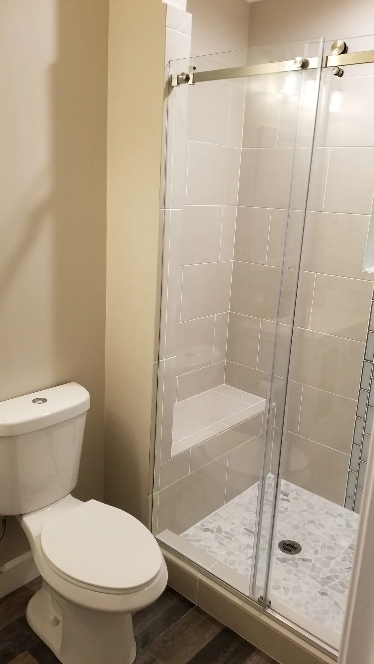 Finished glass-enclosed shower with a tiled bench and mosaic floor
