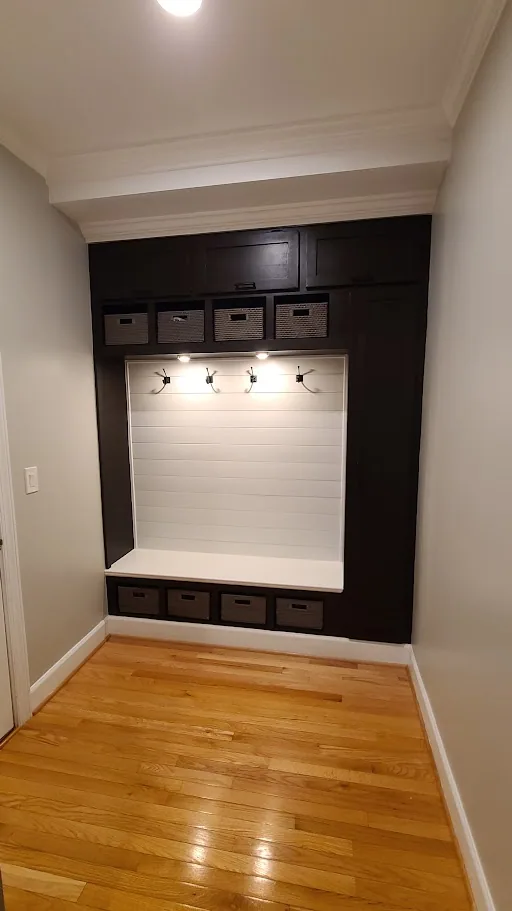 Finished custom mudroom built-in with bench, coat hooks, lighting, and basket storage